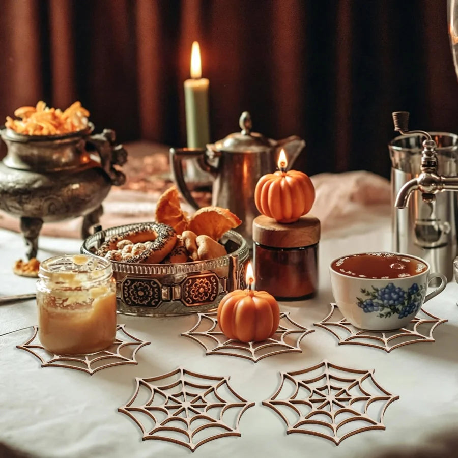A still life featuring wooden spider web ornaments, a lit candle, and a cup of coffee on a white tablecloth.