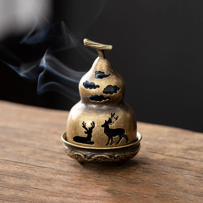 A vintage brass incense burner holder with a deer silhouette and smoke rising on a wooden surface.