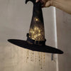 A black witch hat with glowing lights and gold star tassels is hanging.
