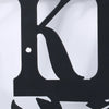 A close-up of a rustic black metal letter K sign mounted on a white wall.