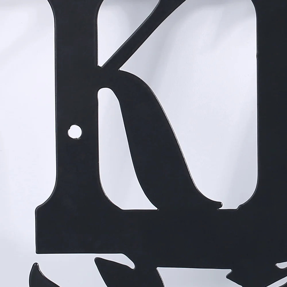A close-up of a rustic black metal letter K sign mounted on a white wall.