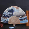 A Japanese foldable hand fan featuring a blue and white Kanagawa wave design against a natural wood background.