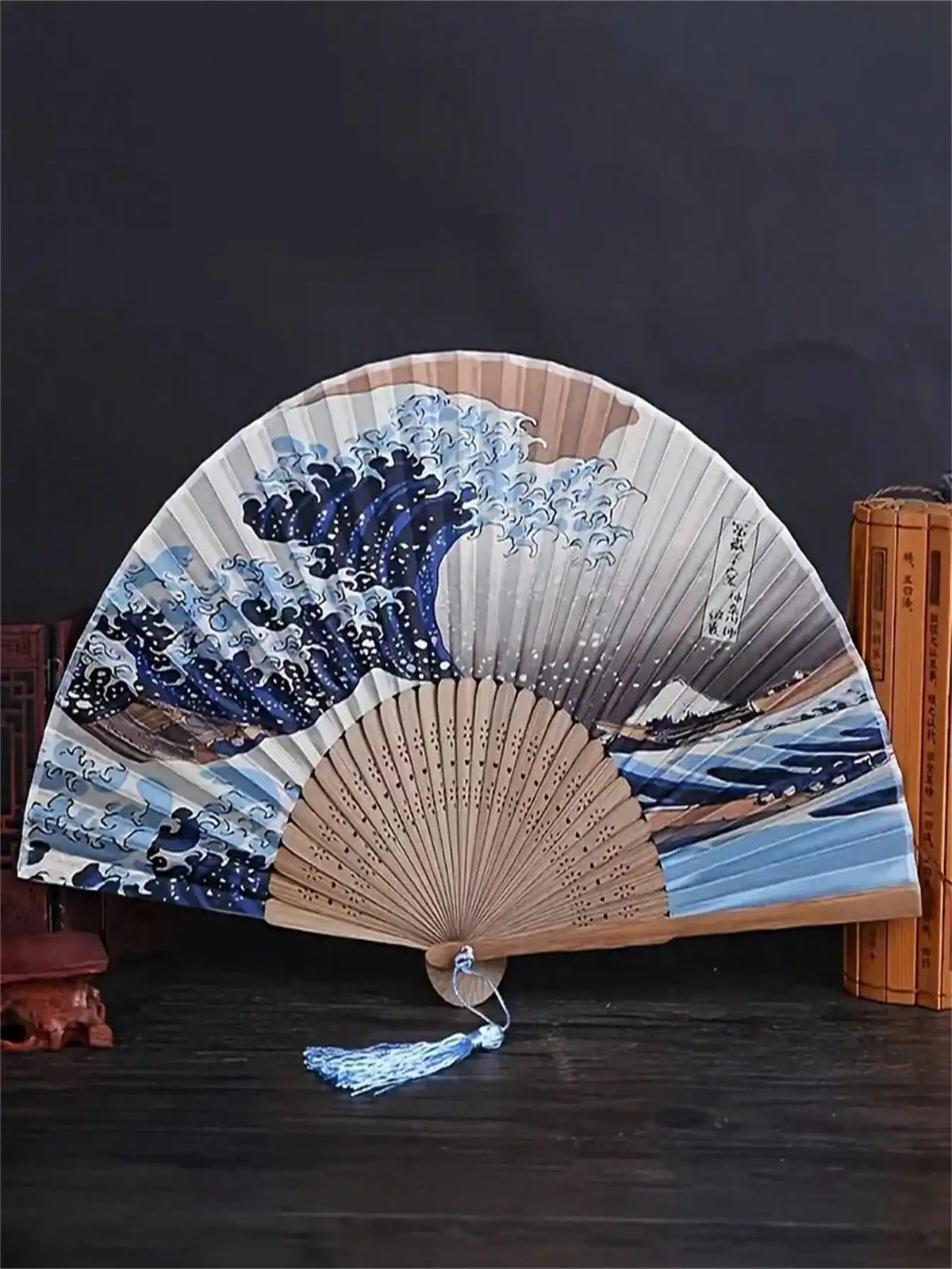 A Japanese foldable hand fan featuring a blue and white Kanagawa wave design against a natural wood background.