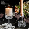 A clear glass pillar candle holder with a pink candle and a wick, set against a dark background.
