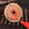 A round, layered knot wall decor made of light beige material with red string and a gold tassel, resting on dark wood.