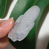 A hand holds a clear silver glitter acrylic charm against a green leaf background.