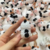 A hand holds a handmade crochet cow keychain featuring black and white patches with pink accents.