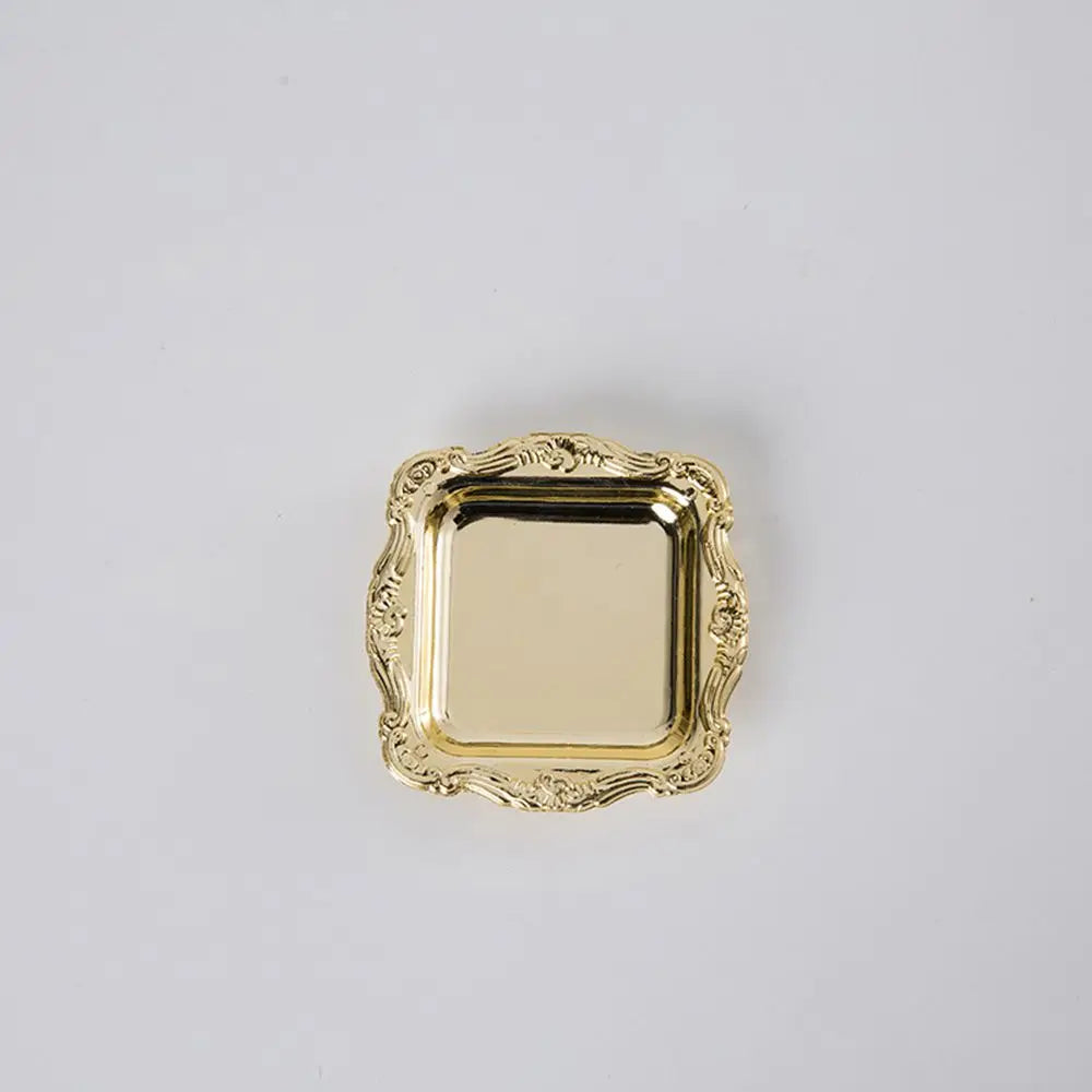 A small, square gold-toned mirror-finish tray with an ornate, ruffled edge.