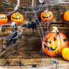A carved orange pumpkin surrounded by fake black spiders and cobwebs on a wooden surface for Halloween decoration.