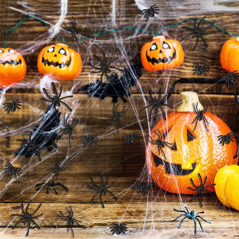 A carved orange pumpkin surrounded by fake black spiders and cobwebs on a wooden surface for Halloween decoration.