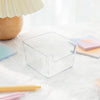 Une boîte de rangement pour bureau en acrylique transparent sur une surface blanche à côté d'un crayon jaune clair et de post
