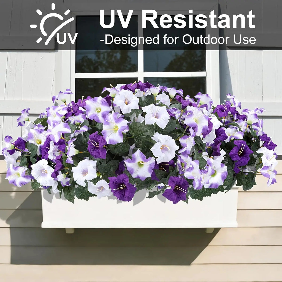 A vibrant arrangement of purple and white artificial petunia flowers with vines displayed in a white planter on a wooden porc