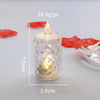 A clear crystal candle holder with a flickering LED light and a pointed top, shown next to red petals.