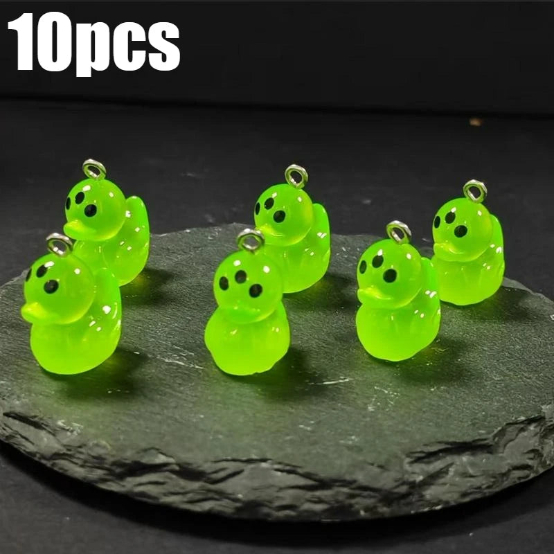 Ten glow-in-the-dark green cartoon alien kitty duck resin charms displayed on a dark surface.