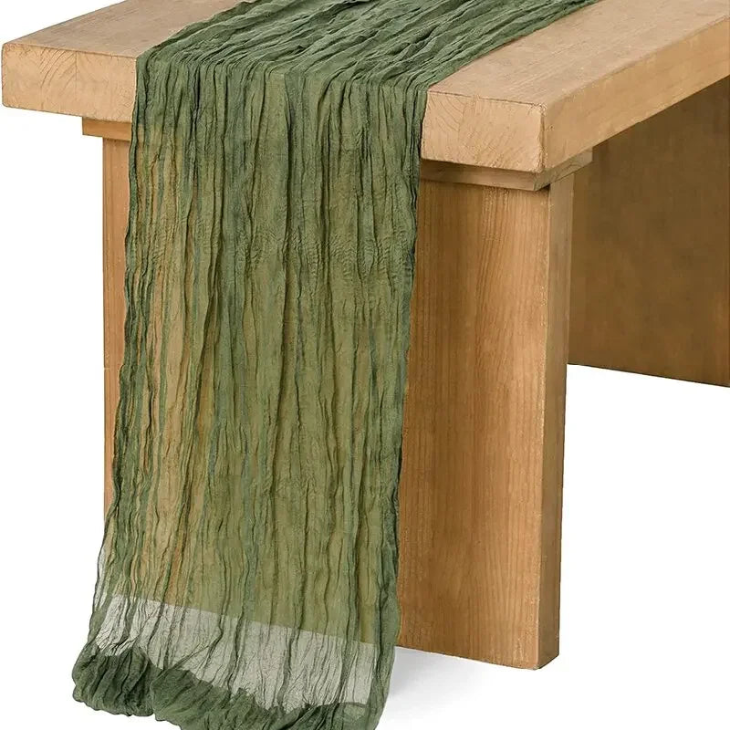 Sage green gauze table runner draped over a light wood table.