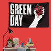 A black banner featuring the text GREEN DAY and a hand holding a heart design with red paint on a red wall.