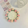 A hand-crocheted bouquet of pink and peach roses used as coasters, displayed next to a glass.