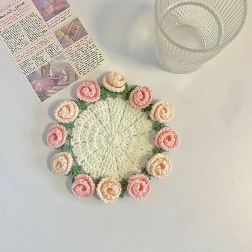 A hand-crocheted bouquet of pink and peach roses used as coasters, displayed next to a glass.