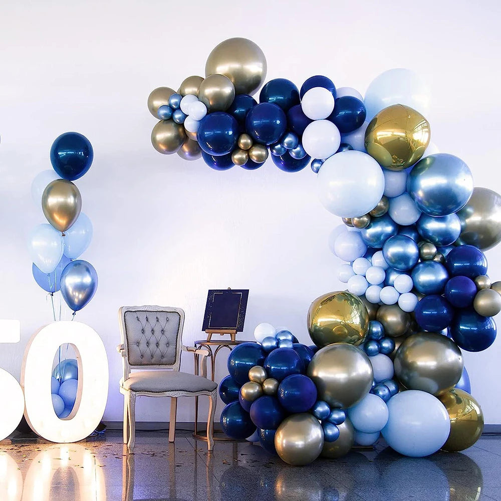 A large balloon garland arch featuring navy blue, gold, and light blue balloons against a white wall.