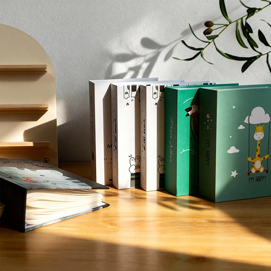 A set of green and white cartoon cover photo albums standing on a wooden surface with sunlight casting shadows.