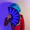 شخص يحمل مروحة ضوئية حريرية LED قابلة للطي تصدر ضوءًا أزرق على خلفية أرجوانية.