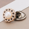 A close-up of a gold-toned pearl and rhinestone no-sew brooch button with a round pearl centerpiece.