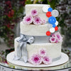 A multi-tiered white cake decorated with pink roses and blue and red foam ball toppers.