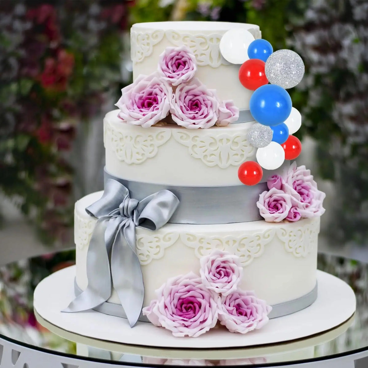 A multi-tiered white cake decorated with pink roses and blue and red foam ball toppers.