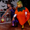 A young girl dressed in a purple witch costume stands next to an adult wearing an orange witch costume, both holding glow-in-