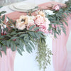 A floral garland featuring pink, cream, and blush roses and green eucalyptus leaves draped on a pink fabric backdrop.