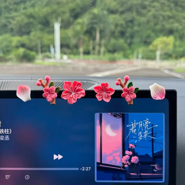 A close-up view of a car dashboard featuring a 3D peach blossom ornament with pink and red flowers.