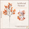 A sprig of artificial orange baby's breath flowers on a dark stem, shown with hands adjusting the branches.