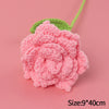 A handmade pink crochet rose flower with green leaves on a light pink background.