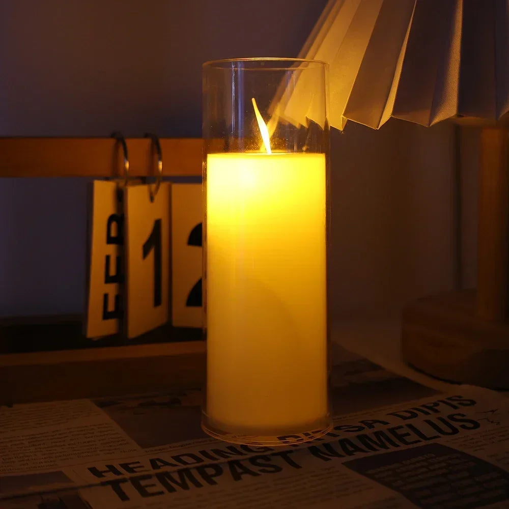 A tall glass candle with a flickering yellow flame is lit in a dimly lit room.