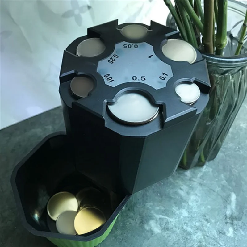A black multi-compartment coin organizer with detachable trays and various sized coins displayed next to a glass container.