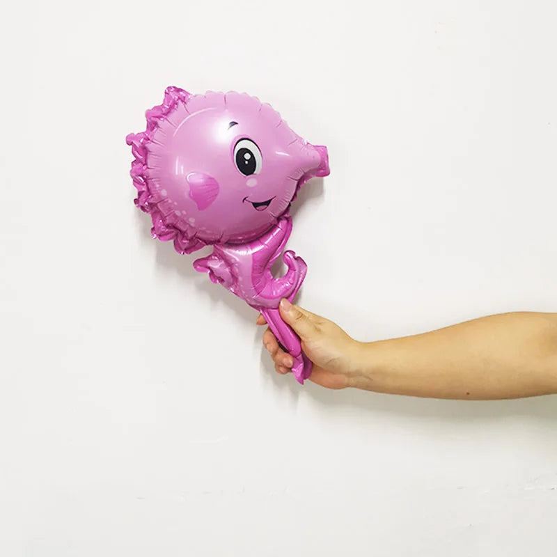 A pink foil balloon shaped like a smiling sea creature is being held against a white wall.