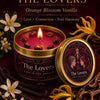 A candle jar labeled The Lovers in orange blossom vanilla with dried botanicals and a yellow floral element.