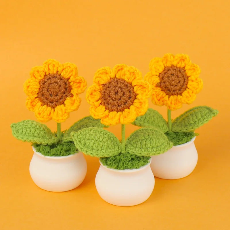 Handmade knitted yellow sunflower with green leaves in a white ceramic pot.