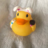 A yellow rubber duck bath toy with white and pink accents is shown on a wrinkled light-colored cloth.