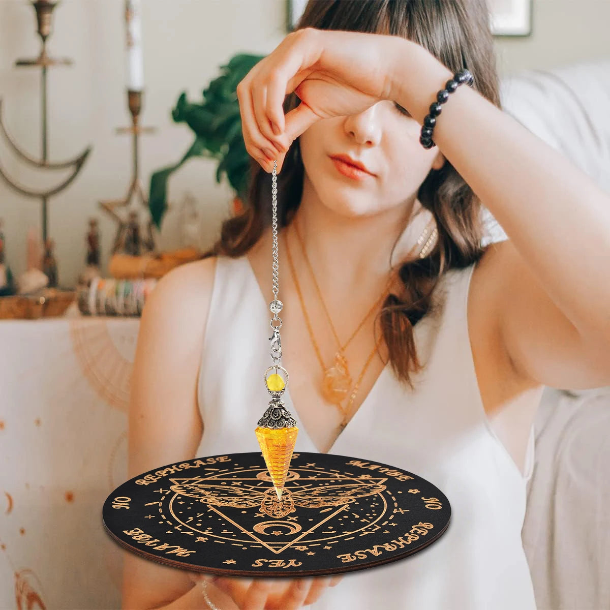 A woman holds a black wooden pendulum board with a yellow crystal pendant and an orange necklace.