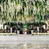 An overhead floral decoration featuring a dense cascade of white wisteria vine garlands and greenery for an event backdrop.