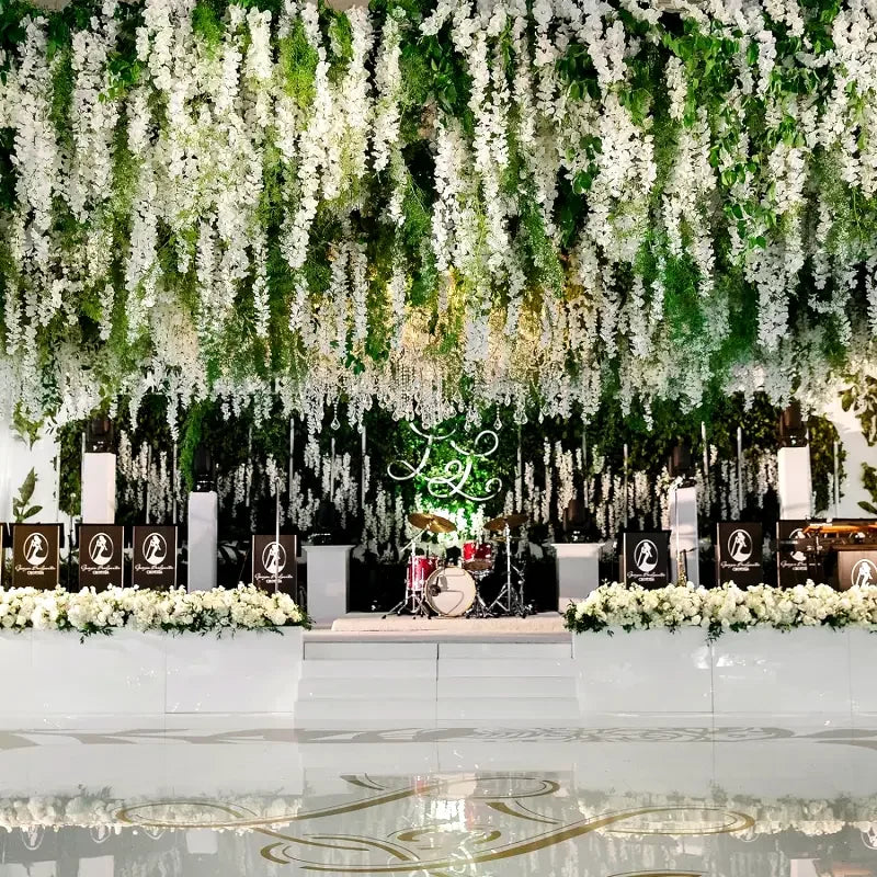 An overhead floral decoration featuring a dense cascade of white wisteria vine garlands and greenery for an event backdrop.