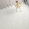A light beige round side table with a vase of pink flowers sits on a white textured rug in a bright room.