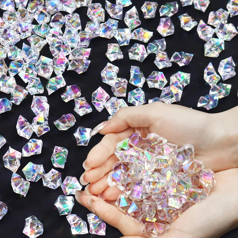 A hand holds a pile of pink and clear decorative crushed diamond acrylic pebbles on a dark surface.