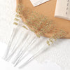 Gold pearl string beads scattered on a wooden surface with white lace fabric.