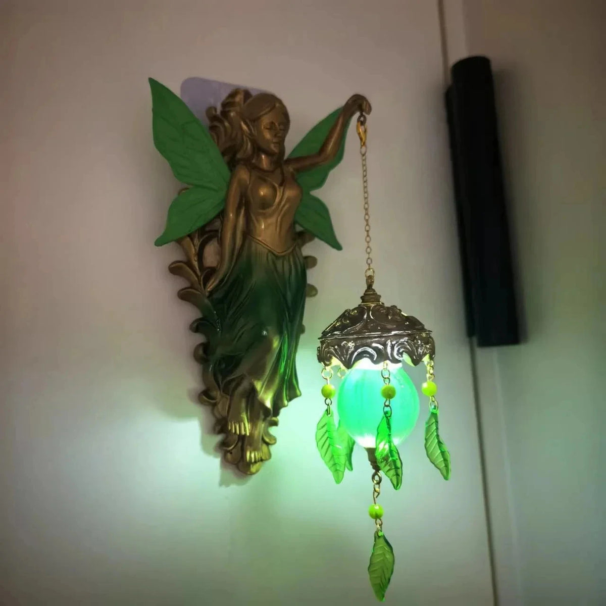 A bronze-finished resin sculpture of a mermaid with green wings hanging as a wall lamp.