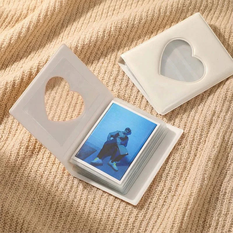 A clear plastic window photocard album with a heart-shaped window and several cards resting on a beige textured fabric.