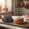 A dark gray nonstick mini fluted cake pan filled with a golden baked cake, set on a wooden cutting board.