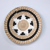 Round woven straw wall decor hanging with concentric black and white patterns