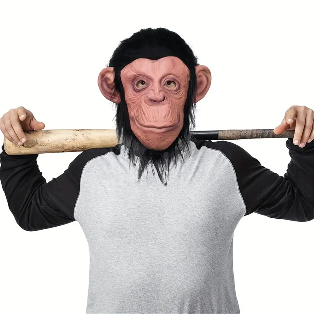 A person wearing a latex monkey mask costume with reddish-brown skin and black hair, holding a wooden stick.